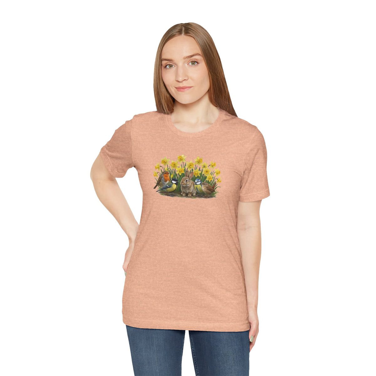 Frau trägt ein peach T-Shirt mit buntem Vogel- und Kaninchen-Motiv in einer Frühlingsumgebung.