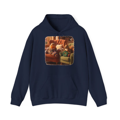 Ein dunkelblauer Kapuzenpullover mit einem quadratischen Grafikdruck auf der Brust, der eine gemütliche Wohnzimmerszene zeigt: Ein Rotkehlchen sitzt neben einem Eichhörnchen im grünen Pullover auf einem Sessel, und beide stricken.