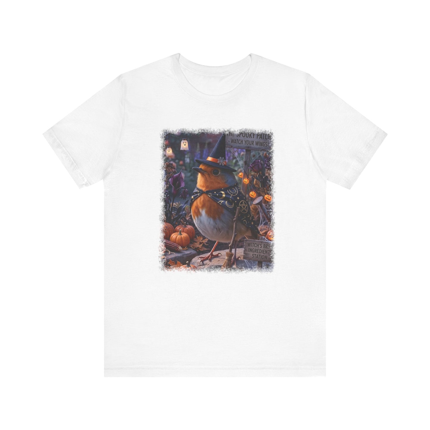 A white short-sleeve crewneck t-shirt featuring a central graphic print of a robin bird dressed as a witch standing among pumpkins and autumn foliage.
