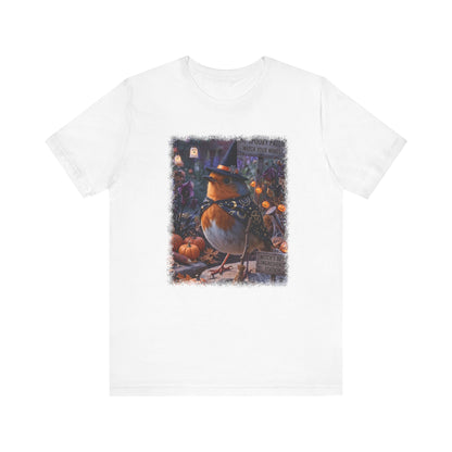 A white short-sleeve crewneck t-shirt featuring a central graphic print of a robin bird dressed as a witch standing among pumpkins and autumn foliage.