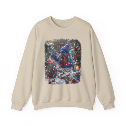 A beige crewneck sweatshirt featuring a square graphic print of a bluebird dressed in a festive red sweater and blue knit hat, surrounded by Christmas lights, pinecones, and snow-covered evergreen trees.