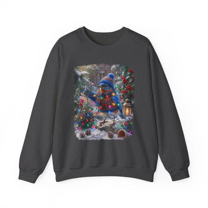 A dark gray crewneck sweatshirt featuring a large square graphic print on the front. The graphic depicts a festive winter scene with a bluebird wearing a blue knit hat and scarf, surrounded by decorated Christmas trees, pinecones, and a lantern in the snow.