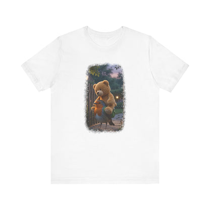 Weißes T-Shirt aus Baumwolle. Auf der Brust ist eine witzige digitale Illustration aufgedruckt: Ein niedliches Rotkehlchen namens Rosi steht im Vorgarten und versucht, einen riesigen Kirmes-Teddybären in einen viel zu kleinen grünen Frosch-Rucksack zu quetschen.