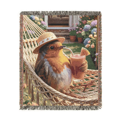 A woven throw blanket featuring a robin bird lounging in a rope hammock, wearing a straw hat and holding a smoothie. The blanket has fringed edges and is shown against a plain white background.