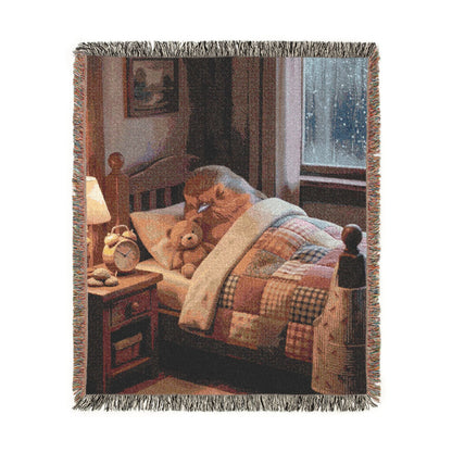 A woven throw blanket with fringed edges, featuring a cozy bedroom scene printed on the front. The design shows a bed with a patchwork quilt, a robin bird, a teddy bear, a bedside table, and a window, all in warm brown, beige, and muted red tones.