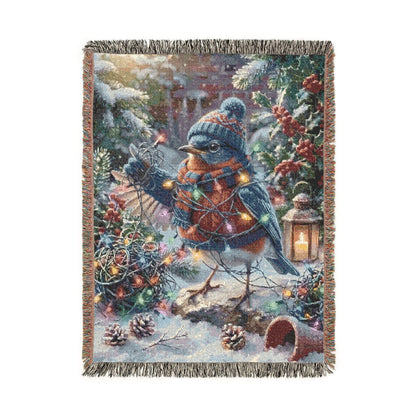 A rectangular woven throw blanket with fringe on all sides, featuring a festive winter scene with bluebirds, evergreen branches, red berries, pinecones, and warm string lights on a white background.