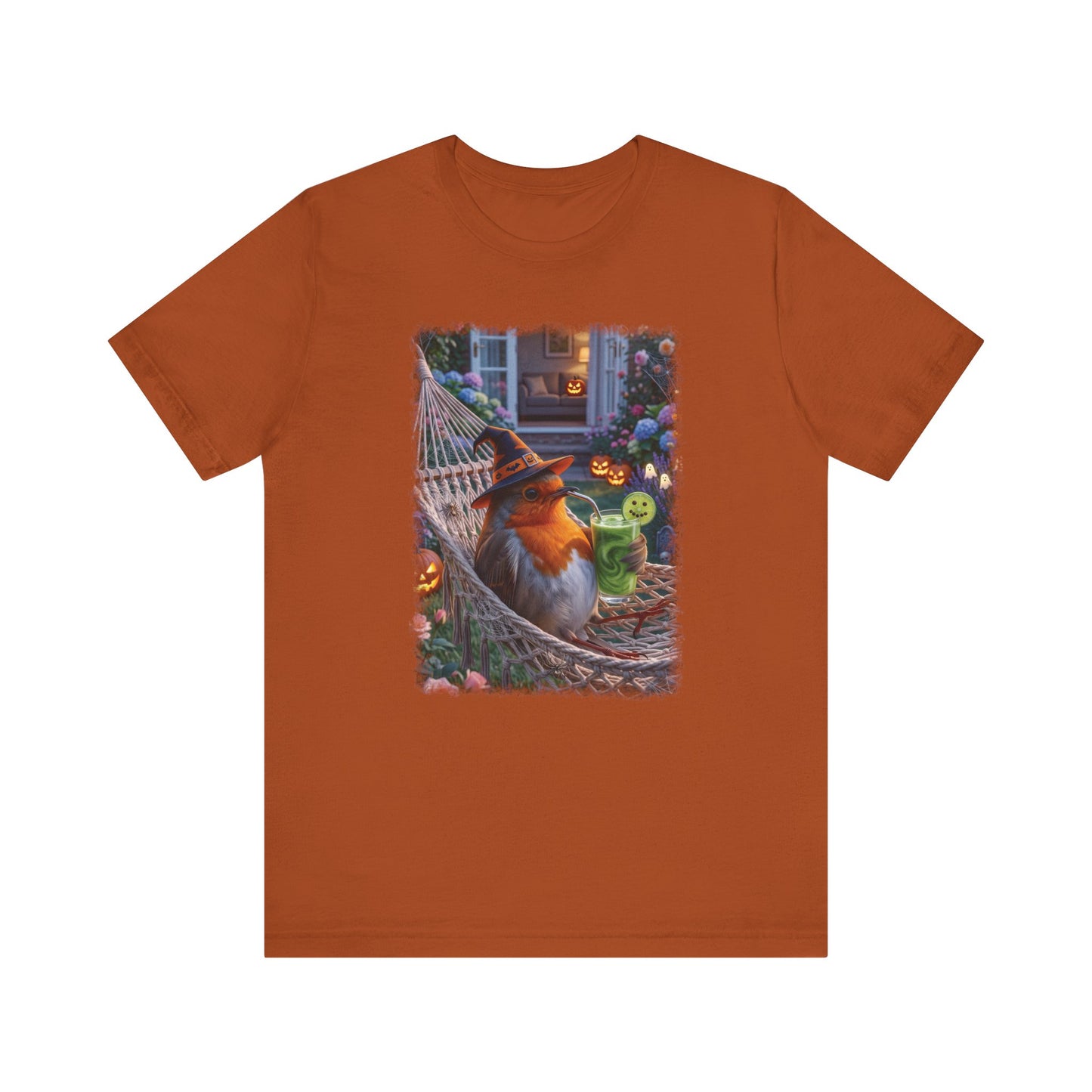 An orange short-sleeve crewneck t-shirt featuring a central graphic print of a robin bird wearing a witch hat sitting in a hammock surrounded by Halloween decorations.