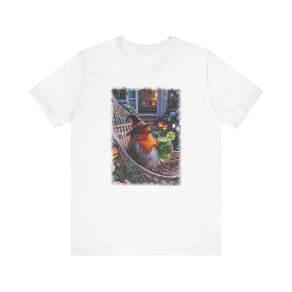 A white short-sleeve crewneck t-shirt featuring a colorful graphic print of a robin bird relaxing in a hammock on a porch during Halloween, surrounded by jack-o'-lanterns and a green drink.