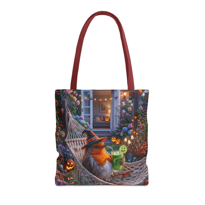 A tote bag with dark red handles, featuring a detailed Halloween-themed illustration of a robin bird in a witch hat relaxing in a hammock surrounded by glowing jack-o'-lanterns and flowers.