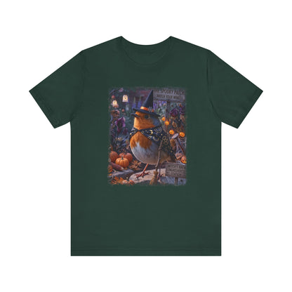 A dark forest green short-sleeve t-shirt with a large, colorful graphic print on the front showing a robin wearing a witch's hat in a spooky pumpkin patch.