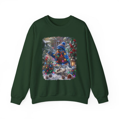 A dark green crewneck sweatshirt featuring a large square graphic print on the front. The graphic depicts a festive winter Christmas scene with a bluebird wearing a knit hat and scarf, perched on a decorated Christmas tree next to a lantern and pinecones.