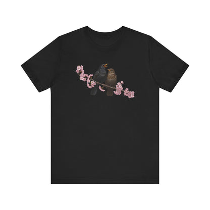 Black t-shirt with a graphic of two birds on a branch with pink flowers on a white background