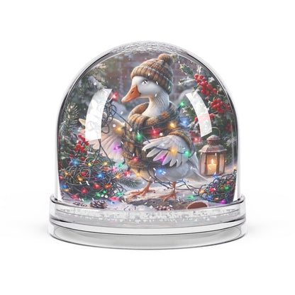 A decorative snow globe featuring a white goose wearing a brown knit hat and scarf, surrounded by a festive Christmas scene with multicolored string lights, evergreen branches, red berries, and a small lantern inside a clear domed globe on a silver base.