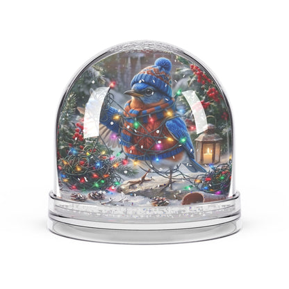 A clear glass snow globe with a silver-toned base, featuring a detailed winter holiday scene inside. The artwork shows a bluebird wearing a blue knit hat and scarf, surrounded by colorful Christmas lights, evergreen trees, snow, and a lantern.