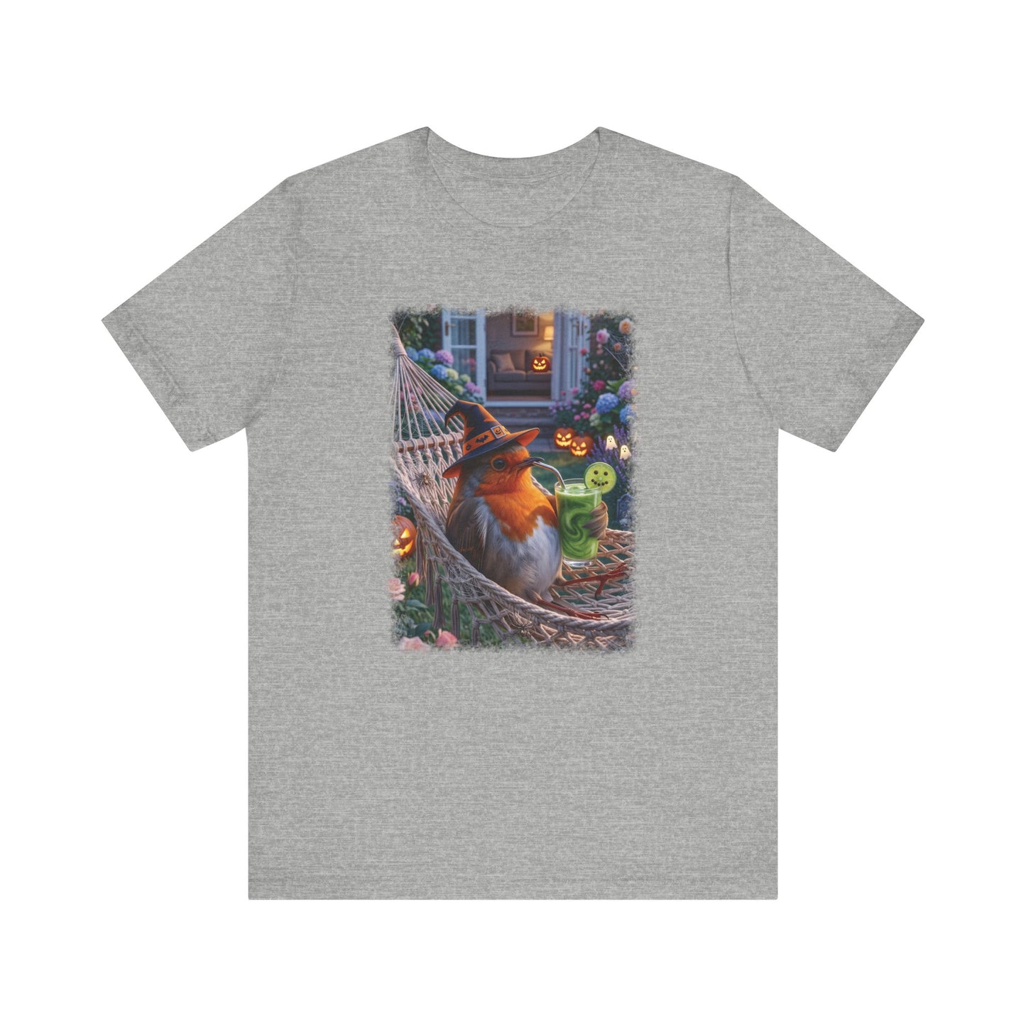 A heather gray short-sleeve crewneck t-shirt featuring a large rectangular graphic print on the front. The graphic depicts a cozy Halloween scene with a fluffy robin bird wearing a witch hat, lounging in a hammock next to a green glowing drink.