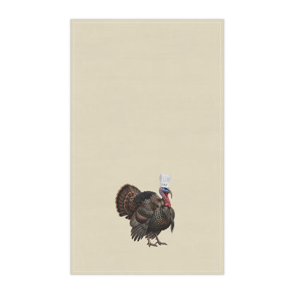 A rectangular beige kitchen towel featuring a small illustrated turkey near the bottom center, wearing a white chef's hat. The product is shown flat against a plain white background.
