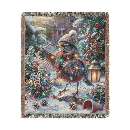 A square woven throw blanket with fringed edges, featuring a detailed winter forest scene with a robin under warm fairy lights, pinecones, evergreen branches, and a lantern, shown on a plain white background.