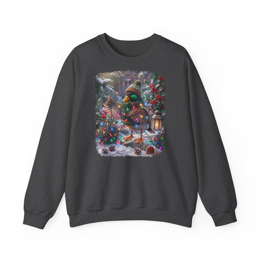 Ein dunkelgraues Sweatshirt mit Rundhalsausschnitt und einem farbenfrohen Grafikdruck: eine Stockente in Winterkleidung und mit Mütze, die inmitten von Weihnachtsbäumen und Schnee eine Lichterkette hält.