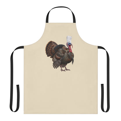 A beige apron with black neck and waist straps, featuring a central graphic of a wild turkey wearing a chef's hat and holding a spatula, set against a plain white background.