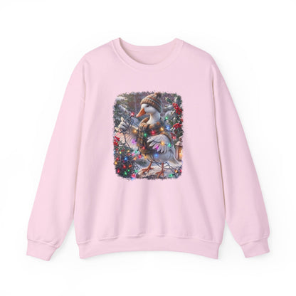 A light pink crewneck sweatshirt featuring a square graphic print on the chest of a snowy goose wearing a knit hat and scarf, surrounded by festive greenery and red berries.