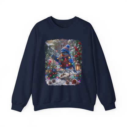 A navy blue crewneck sweatshirt featuring a large, colorful square graphic print on the front. The graphic depicts a festive winter scene with a bluebird in a blue knit hat and scarf, wrapped in warm holiday lights, standing in a snowy garden decorated with Christmas trees and pinecones.