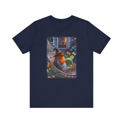 A navy blue short-sleeve crewneck t-shirt featuring a colorful graphic print of a robin bird wearing a witch hat and sitting in a hammock surrounded by Halloween decorations.