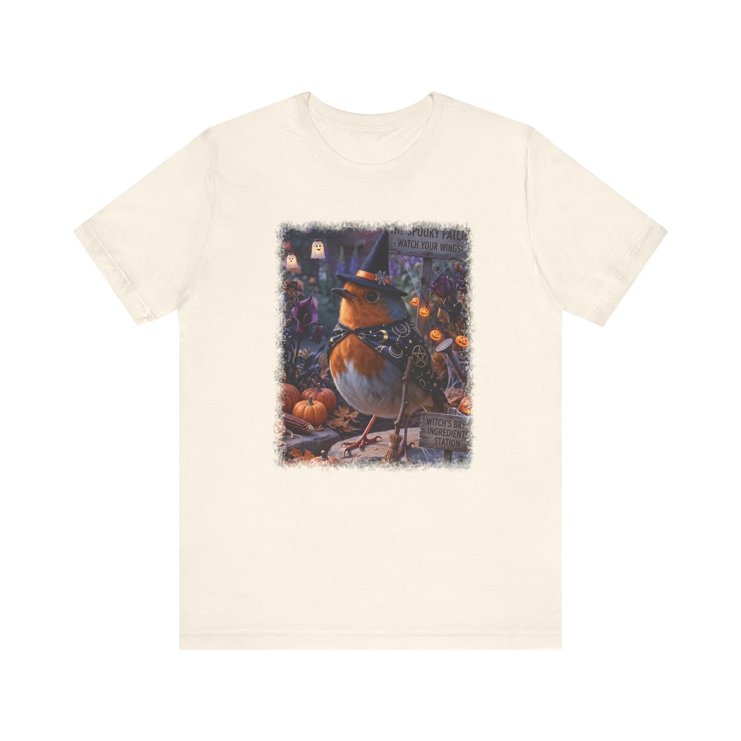 An off-white crewneck t-shirt featuring a colorful graphic print of a robin dressed as a witch surrounded by pumpkins on a white background.