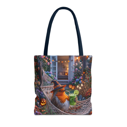A tote bag with dark navy blue handles, featuring a detailed Halloween-themed illustration on the front. The artwork shows a robin bird wearing a witch hat lounging in a hammock surrounded by glowing jack-o'-lanterns and flowers.
