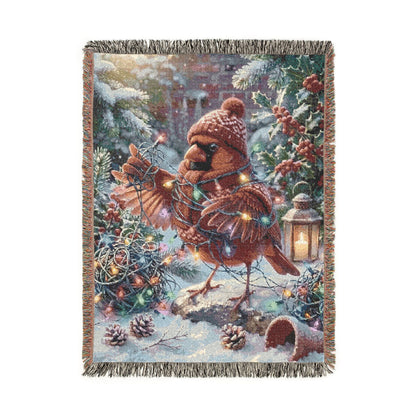 A rectangular woven throw blanket with fringed edges, featuring a whimsical winter holiday scene with a cardinal bird, evergreen branches, pinecones, ornaments, and a lantern on a snowy background.