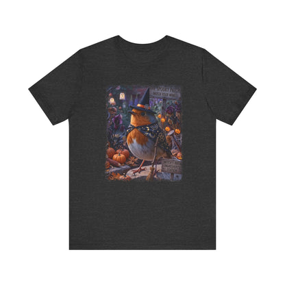A dark heather gray short-sleeve t-shirt with a colorful graphic print of a robin wearing a witch hat surrounded by pumpkins and autumn foliage, displayed on a solid white background.