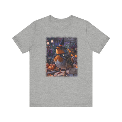 A heather gray short-sleeve crewneck t-shirt featuring a colorful graphic print of a robin dressed as a witch sitting among pumpkins on a porch.