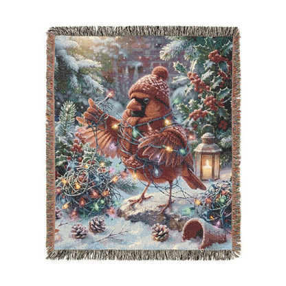A woven throw blanket with fringed edges, featuring a festive Christmas winter scene with a cardinal bird, pine trees, snow, evergreen branches, berries, and warm string lights, shown on a plain white background.