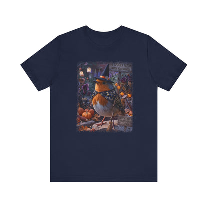 A navy blue short-sleeve crewneck t-shirt featuring a detailed graphic print of a robin wearing a witch hat in a spooky autumn setting with pumpkins and lanterns.