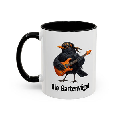 Tasse mit einer Amsel, die Gitarre spielt, und dem Text „Die Gartenvögel“ auf weißem Hintergrund