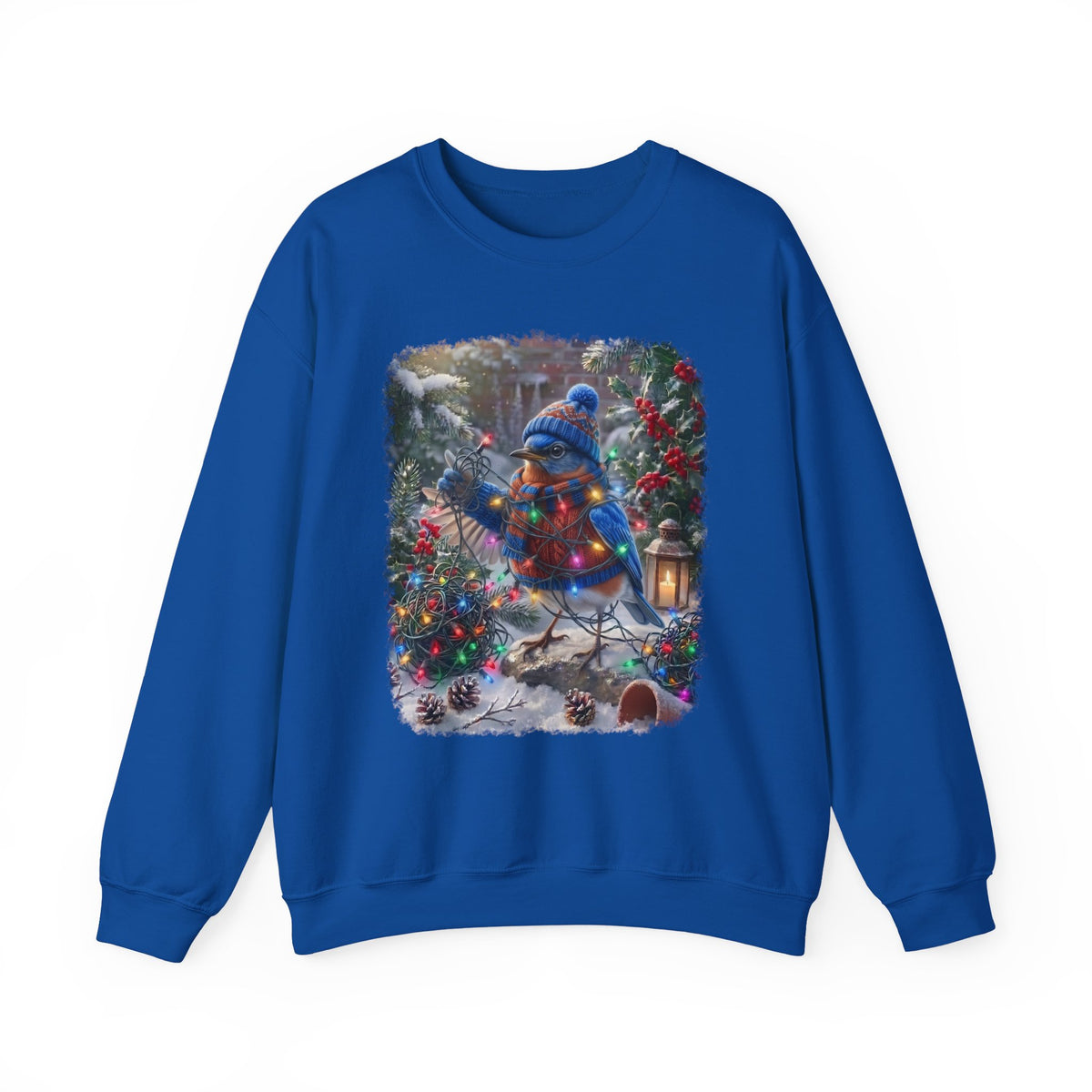 A royal blue crewneck sweatshirt featuring a large square graphic print on the front of a snowy Christmas tree scene with a bluebird, ornaments, and warm lights.