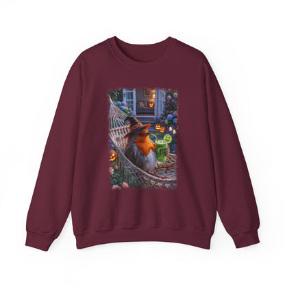 A maroon crewneck sweatshirt featuring a large graphic print on the front of a robin bird wearing a witch hat and sitting in a hammock surrounded by Halloween decorations.
