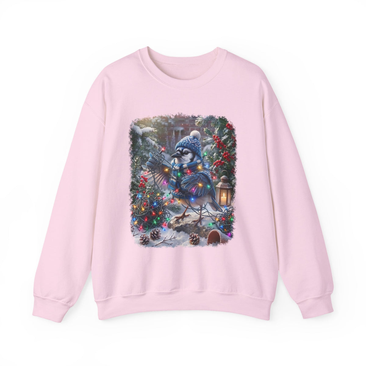 A light pink crewneck sweatshirt featuring a large, colorful graphic print of a blue jay wearing a winter hat and scarf, surrounded by Christmas trees and ornaments in a snowy outdoor scene.