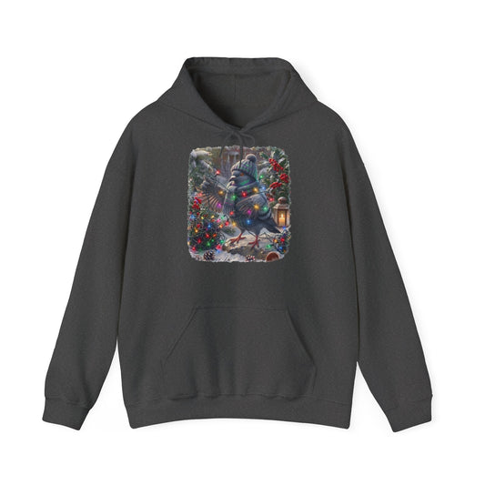 Ein dunkelgrauer Kapuzenpullover und einem farbenfrohen Grafikdruck: eine Taube in Winterkleidung und mit Mütze, die inmitten von Weihnachtsbäumen und Schnee eine Lichterkette hält.