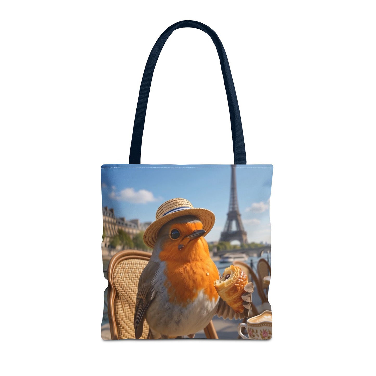 A tote bag with dark navy blue handles, featuring a printed graphic of a robin wearing a straw hat and holding a croissant with the Eiffel Tower in Paris in the background.