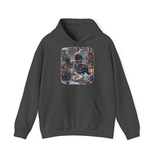 Ein dunkelgrauer Kapuzenpullover und einem farbenfrohen Grafikdruck: eine Amsel in Winterkleidung und mit Mütze, die inmitten von Weihnachtsbäumen und Schnee eine Lichterkette hält.