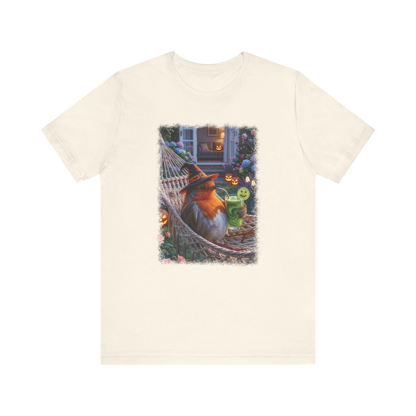 An off-white short-sleeve crewneck t-shirt featuring a colorful graphic print of a robin bird relaxing in a hammock surrounded by pumpkins and a green frog on a mug, displayed against a solid white background.