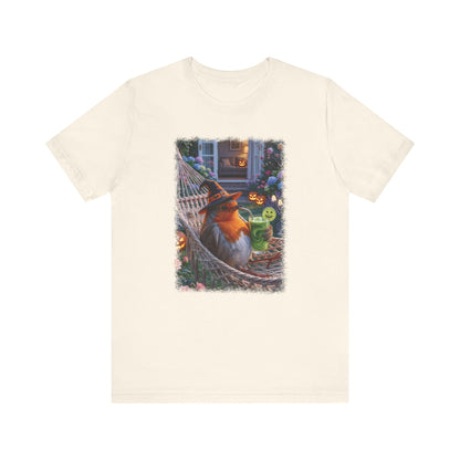 An off-white short-sleeve crewneck t-shirt featuring a colorful graphic print of a robin bird relaxing in a hammock surrounded by pumpkins and a green frog on a mug, displayed against a solid white background.