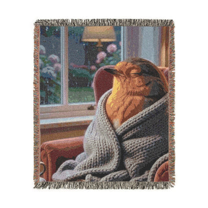 A woven throw blanket with fringed edges, featuring a cozy scene of a robin bird wrapped in a gray knit blanket and looking out a window. The background of the scene is dark, while the foreground and blanket are in soft focus.