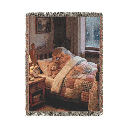 A rectangular woven throw blanket with fringed edges, featuring a printed scene of a cozy bedroom with a patchwork quilt, bed, a sleeping robin bird, a teddy bear, window, and warm-toned furniture. The blanket is shown against a plain white background.