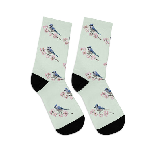 A pair of comfortable sage green socks featuring a seamless all-over print pattern of a vibrant Blue Jay and delicate cherry blossoms. Eco-friendly birdwatching apparel.