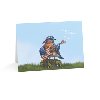 Greeting card with a bluebird playing an American flag guitar on a grassy background