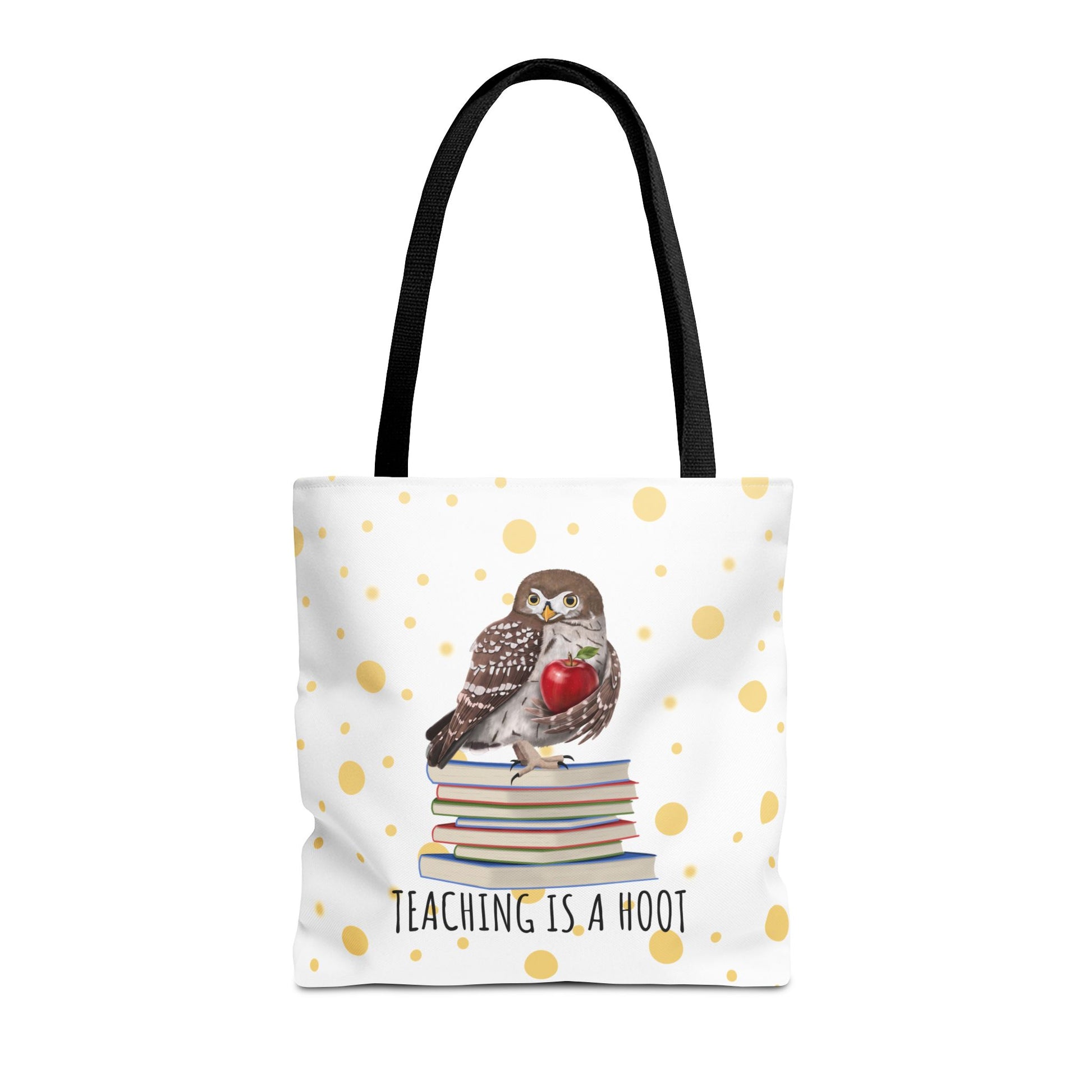 A white tote bag with black shoulder straps, featuring a printed design of a small owl perched on a stack of books and holding a red heart, with the text 'TEACHING IS A HOOT' below. The bag is decorated with scattered gold polka dots on a white background.