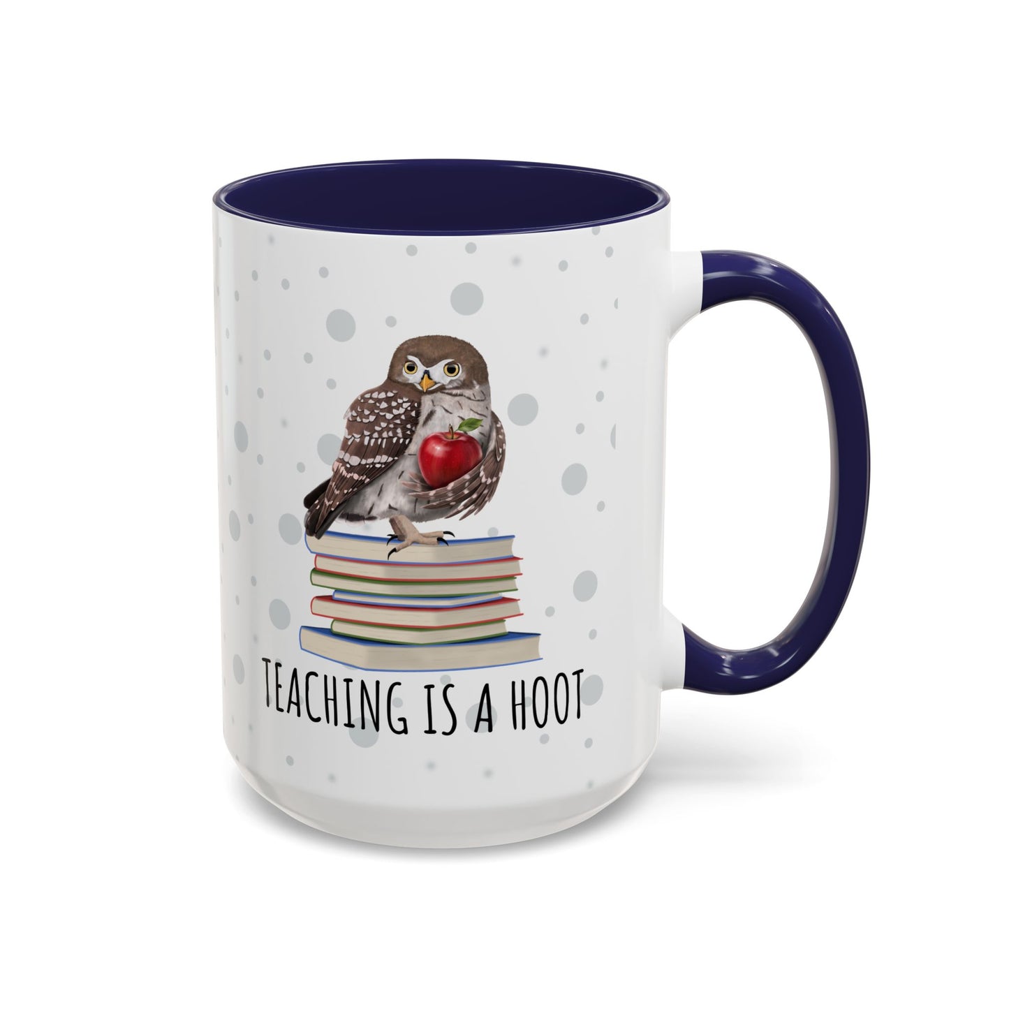A white ceramic mug with a navy blue interior and handle, featuring a printed illustration of an owl perched on a stack of books holding a red apple, with the text 'TEACHING IS A HOOT' below.