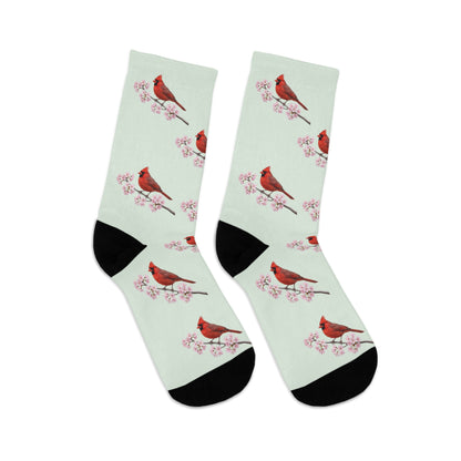 A pair of comfortable sage green socks featuring a seamless all-over print pattern of a vibrant Northern Cardinal and delicate cherry blossoms. Eco-friendly birdwatching apparel.