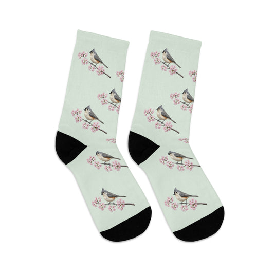 A pair of comfortable sage green socks featuring a seamless all-over print pattern of a vibrant Tufted Titmouse and delicate cherry blossoms. Eco-friendly birdwatching apparel.